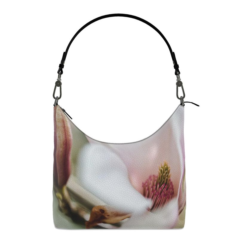 White magnolia flower with hues of soft pinks and greens on a leather hobo bag with a black strap.