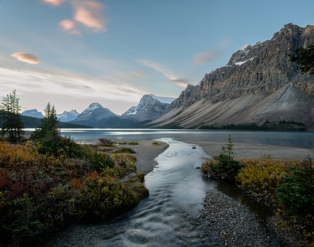 Sunrise landscape of Bow Lake in Banff National Park with a small stream flowing into the lake and rugged mountain peaks rising in the distance.