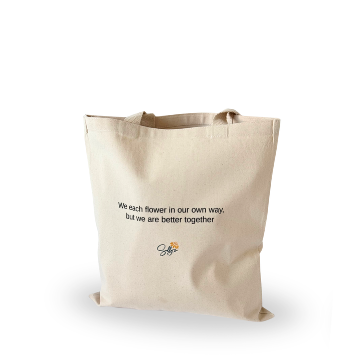Back of natural canvas tote featuring the inspirational message, “We each flower in our own way, but we are better together.”