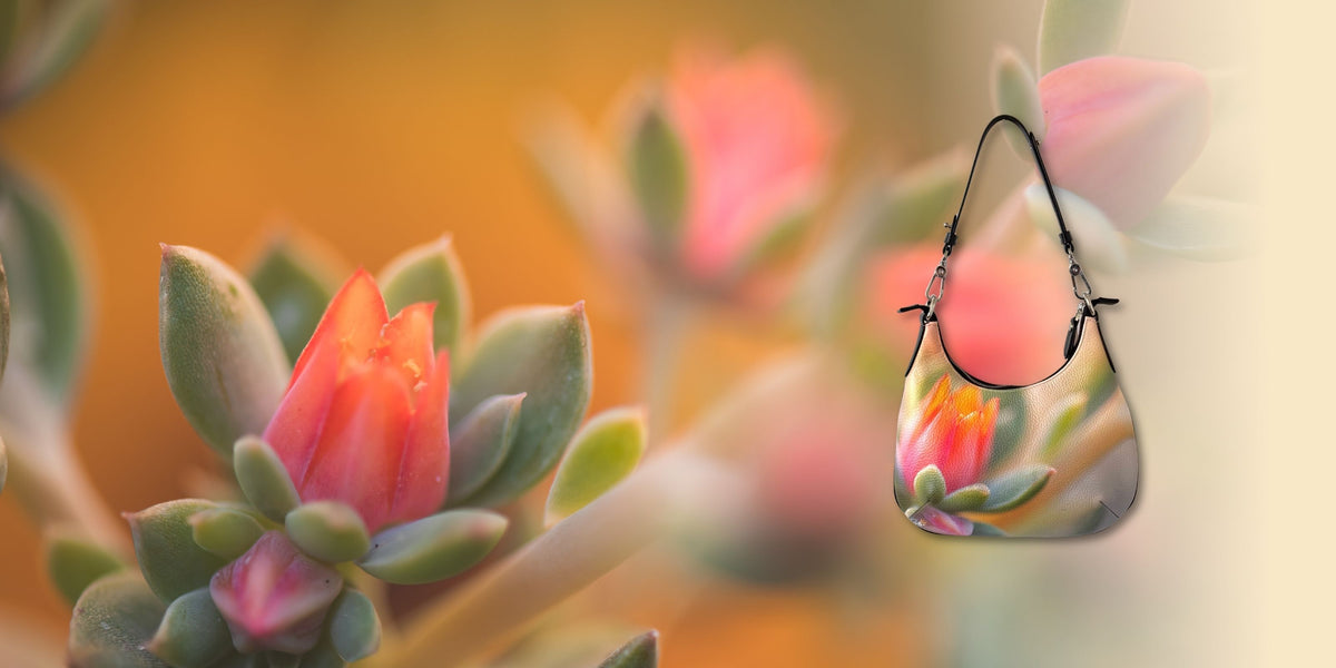 Textured shoulder bag with coral and pink flower artwork, shown against a softly blurred garden background.