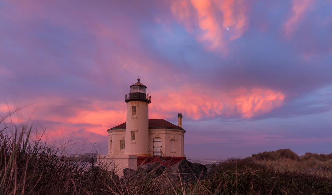 Coquille River Lighthouse at sunrise at Coquille Point near Bandon Oregon with pink and violet clouds and the moon visible above the lighthouse.