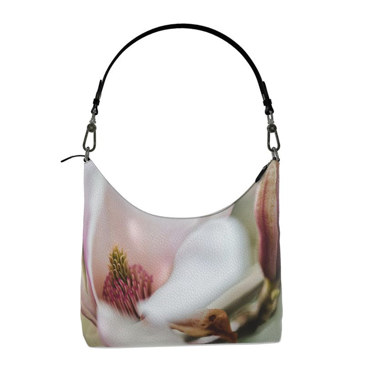 White magnolia flower with hues of soft pinks and greens on a leather hobo bag with a black strap.