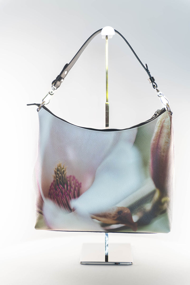 White Magnolia flower with shades of pinks and greens on a leather hobo bag with a white background.