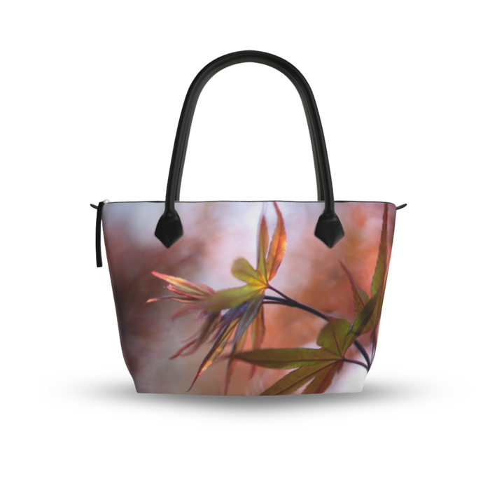 Maple leaf zip top handbag with warm autumn tones of red, orange, and green leaves in soft focus, structured silhouette with black leather handles and top zipper closure, nature inspired design by Sally Halvorsen. Crafted in London. Monroe Satin