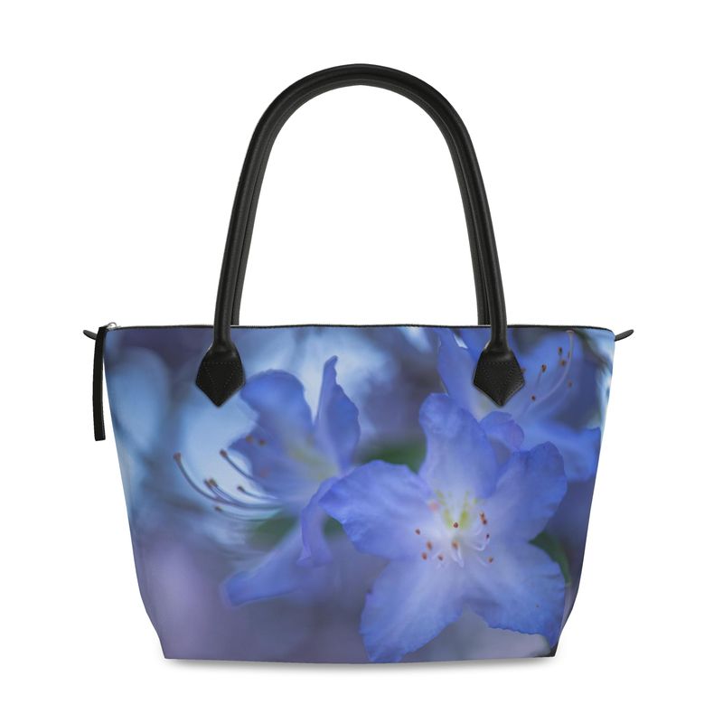 Rhododendron flower zip top handbag featuring a soft blueish purple blossom with layered petals and a gentle green blurred background, structured silhouette with black leather handles and top zipper closure, botanical art design by Sally Halvorsen in Monroe Satin.