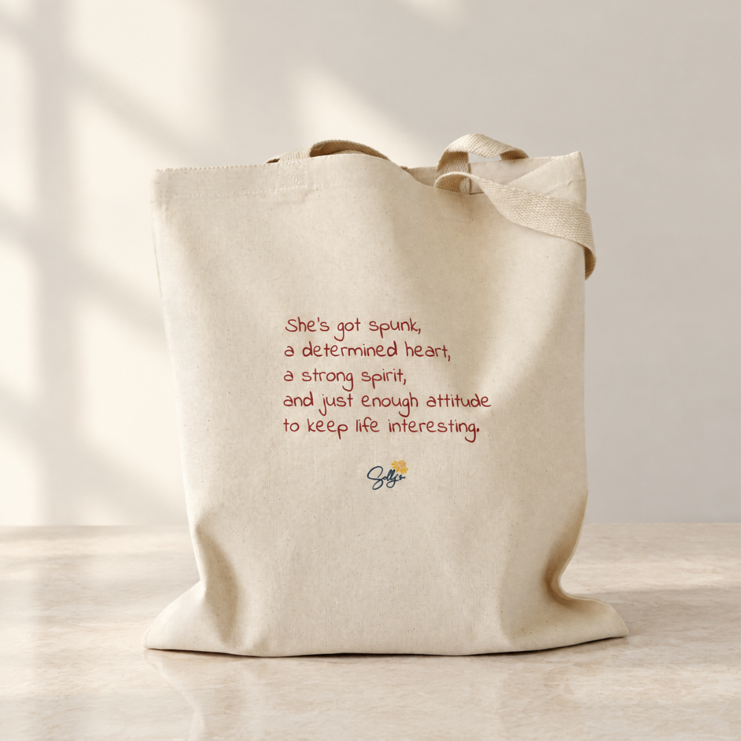 Back of She’s Got Spunk natural canvas tote with red text reading, “She’s got spunk, a determined heart, a strong spirit, and just enough attitude to keep life interesting,” above Sally’s Blooming Bags logo.