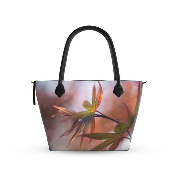 Maple leaf zip top handbag with warm autumn tones of red, orange, and green leaves in soft focus, structured silhouette with black leather handles and top zipper closure, nature inspired design by Sally Halvorsen. Monroe Satin