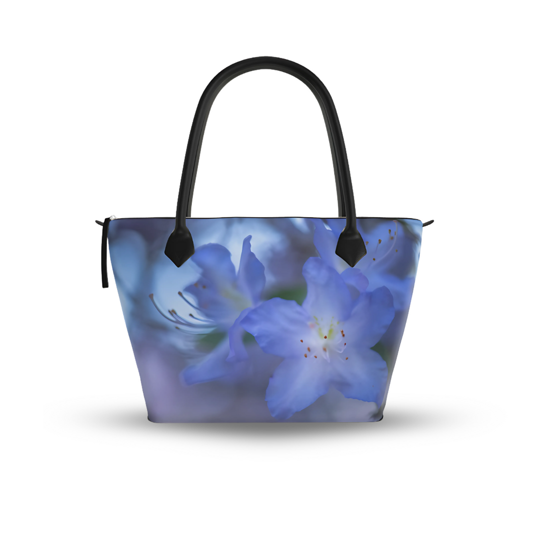 Zip-top tote bag with black leather handles featuring a soft blue rhododendron flower design on a muted background in smooth nappa leather
