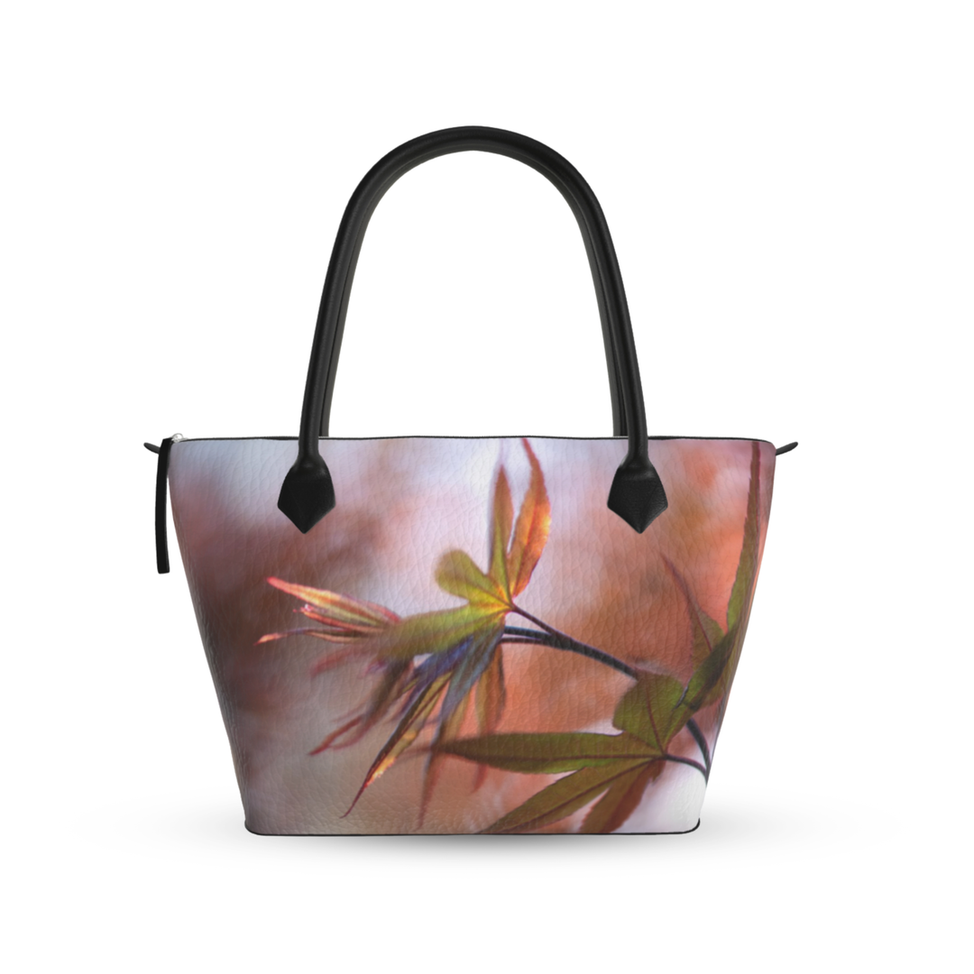 Maple leaf zip top handbag with warm autumn tones of red, orange, and green leaves in soft focus, structured silhouette with black leather handles and top zipper closure, nature inspired design by Sally Halvorsen. Textured Nappa Leather