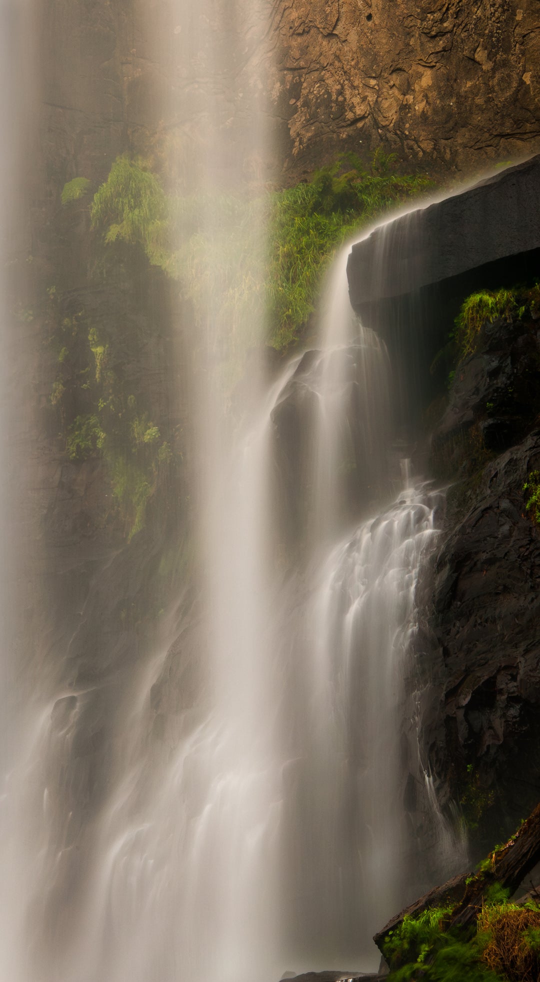 Long exposure waterfall in Oregon with soft flowing water cascading over dark rock shelves and moss-covered stone.